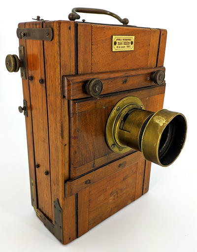 Фотокамера со штативом. Одна из ранних студийных фотокамер. На объективе ещё отсутствует механический затвор с выдержкой съемки.