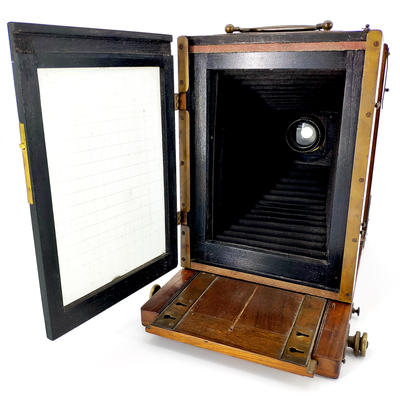 Фотокамера со штативом. Одна из ранних студийных фотокамер. На объективе ещё отсутствует механический затвор с выдержкой съемки.