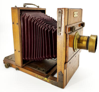 Фотокамера со штативом. Одна из ранних студийных фотокамер. На объективе ещё отсутствует механический затвор с выдержкой съемки.